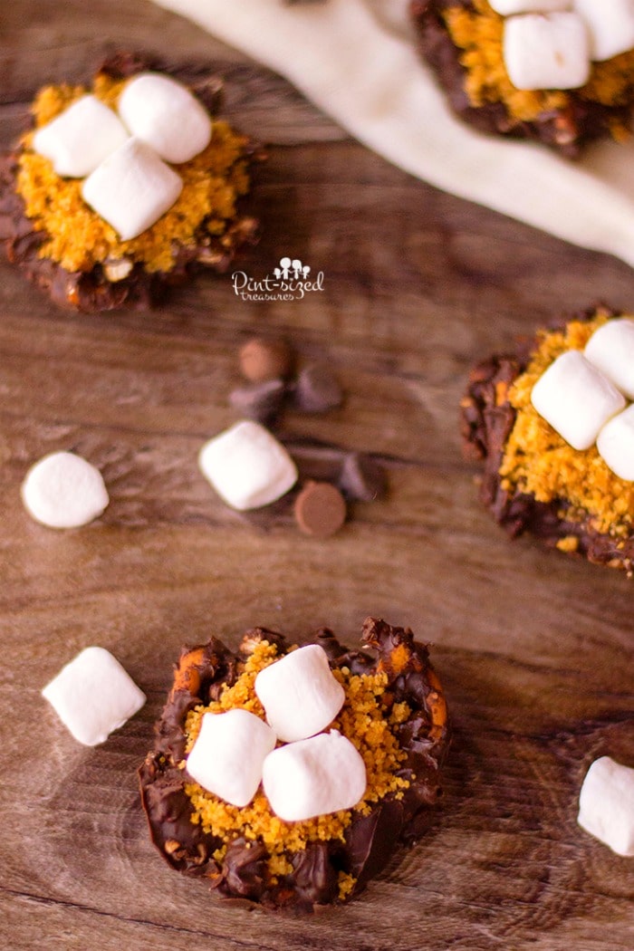 Chopped pretzels are coated with chocolate, placed in tins and topped with additional chocolate, graham cracker crumbs and mini marshmallow to create a crazy yummy, sweet and salty pretzel s'mores bites recipes! Perfect for s'mores fans! #pretzelsmores #smores #Easysmores #nobakesmores #sweetadnsaltysmores #pretzeltreats #easytreats #easydessert #easydessertrecipe