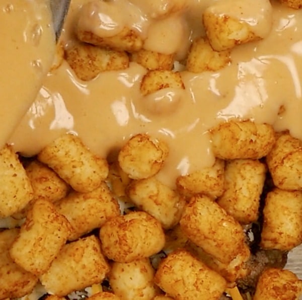 pouring mixture over tater tots for casserole