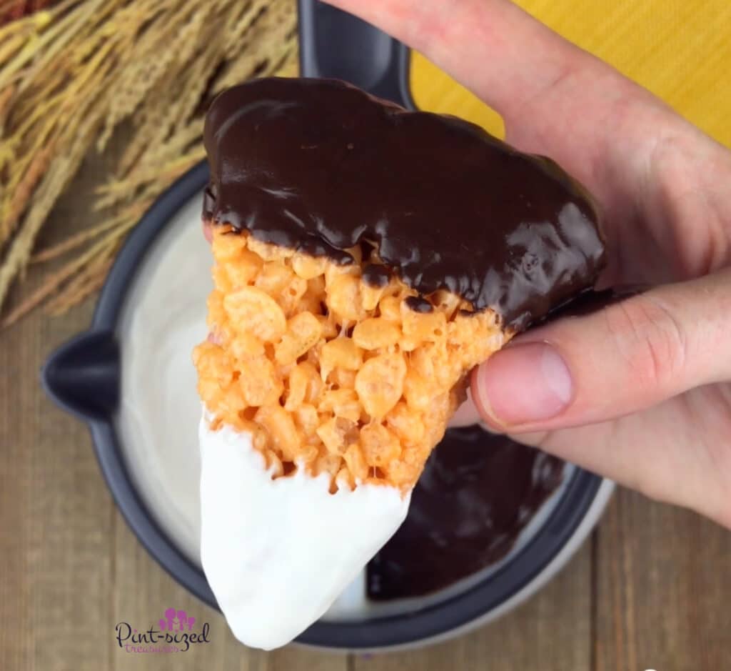 candy corn treat being dipped into dark and white chocolate