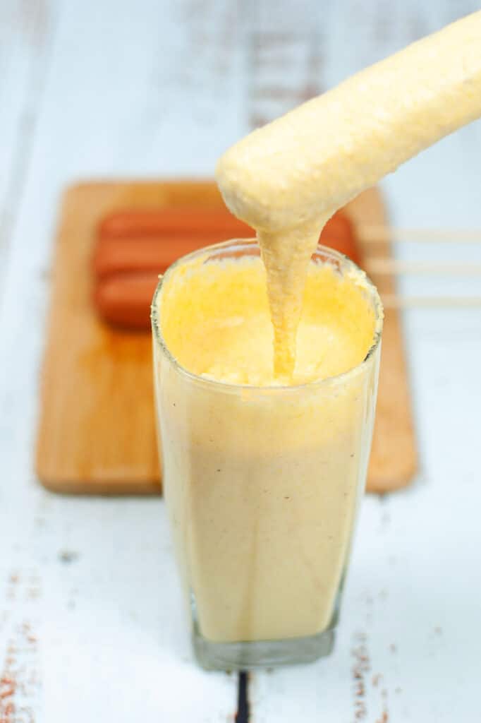 dipping hotdogs to make homemade corn dogs