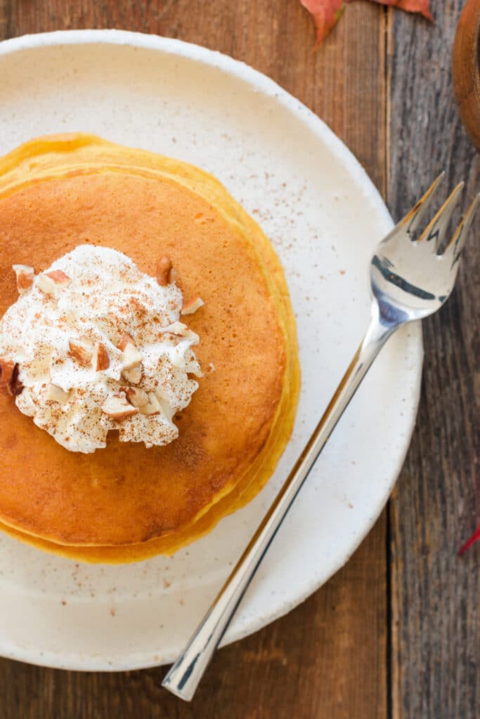 pumpkin pancakes with whipped cream on white plate