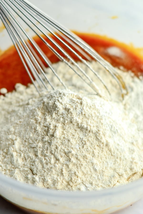 adding flour to pumpkin batter for pumpkin muffins