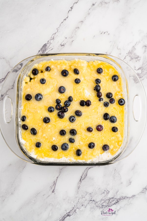 adding butter, cake mix, and blueberries to pan for blueberry dump cake