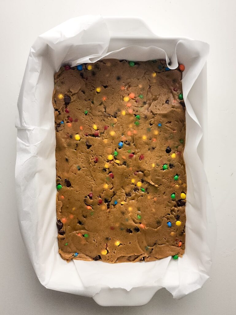 Cookie dough mixed with M&Ms spread out in baking dish